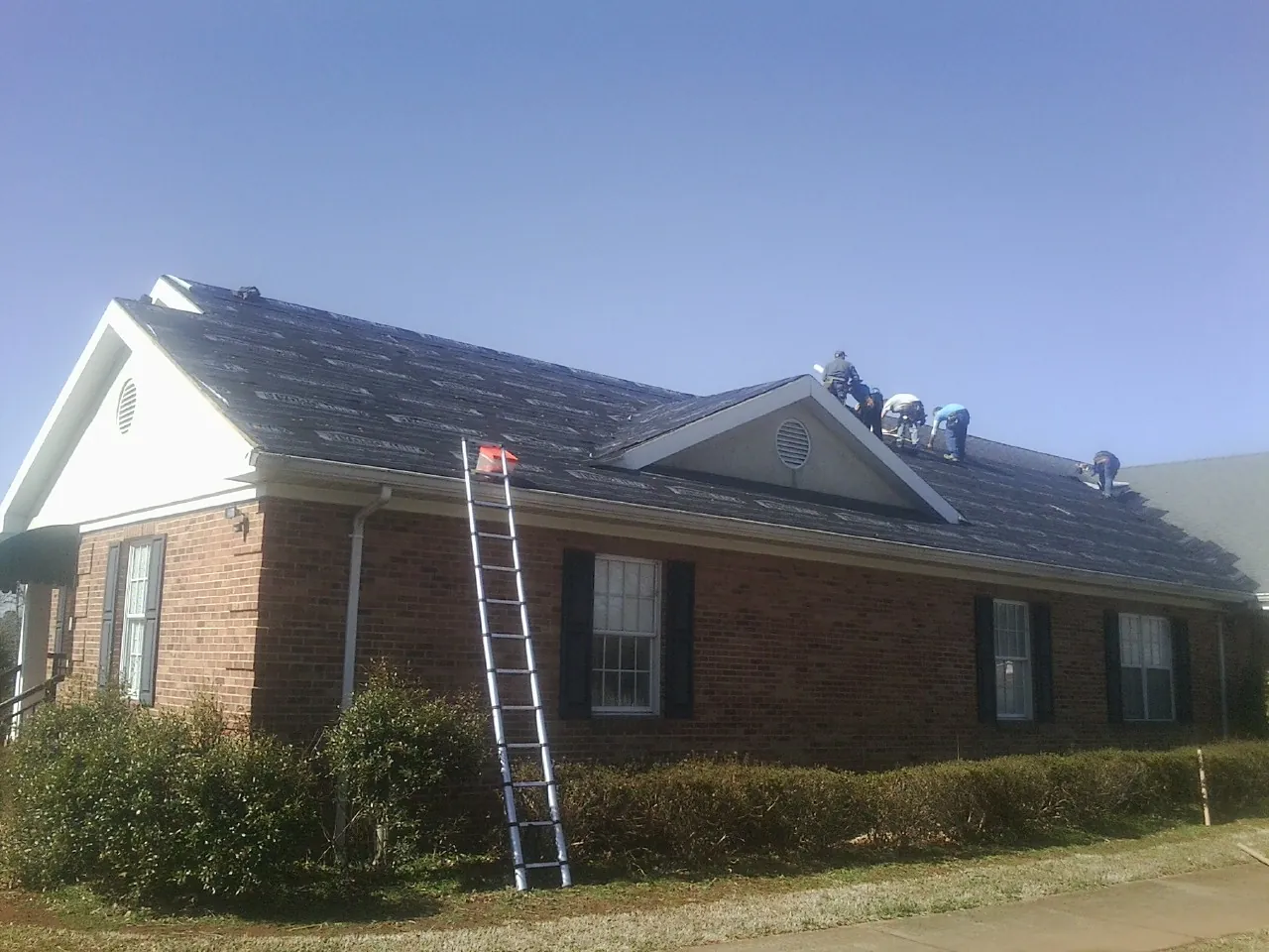 Crew tearing shingles off a brick ranch roof with a ladder set — Emergency Roof Repair work by our crew in Heyburn