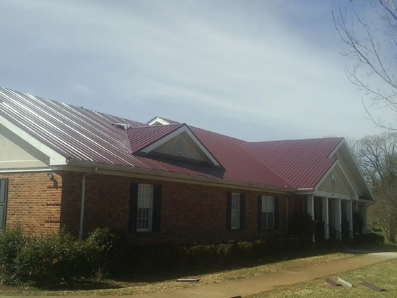 Red metal roof with gabled entries on a long brick building, from a Hail Damage Roof Repair job in Heyburn