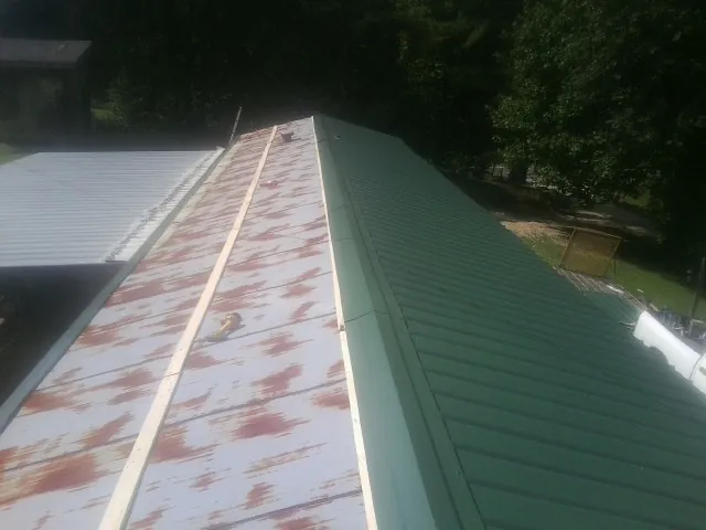 Old rusted panels beside newly installed green metal roofing — Wind Damage Roof Repair by Roofing Brothers in Heyburn