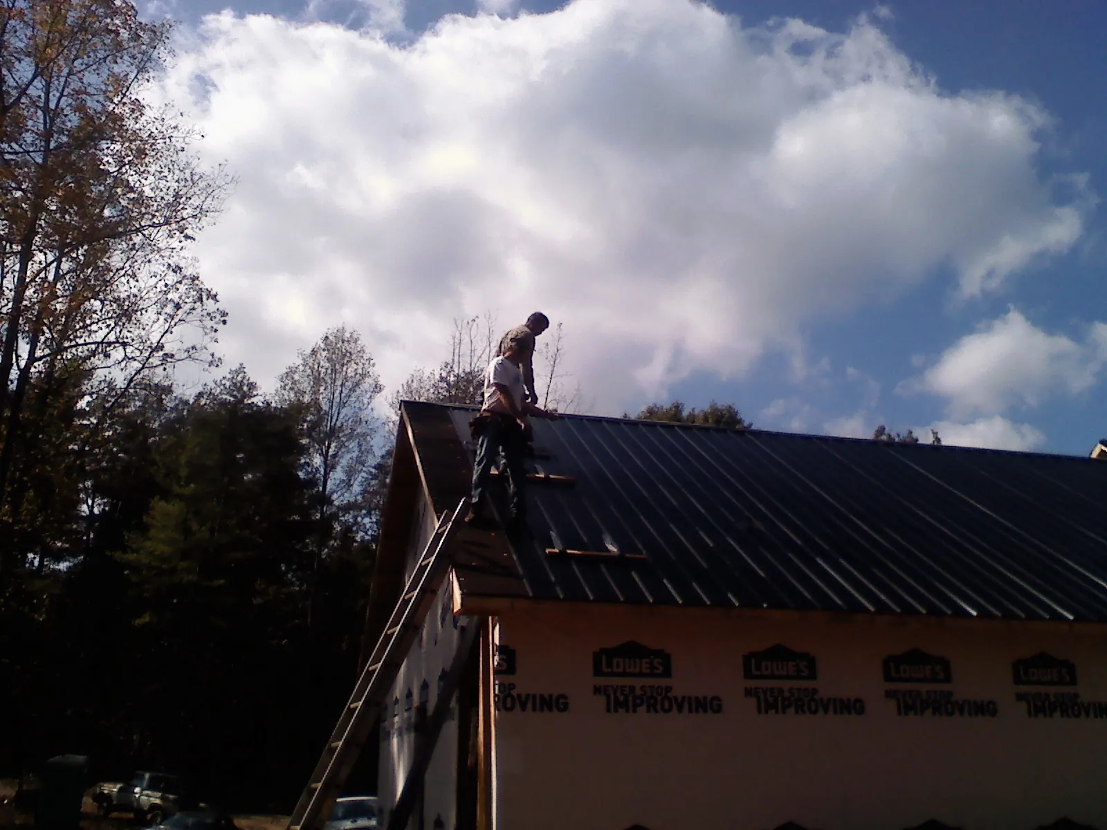 Roofer fastening dark metal panels high against a cloudy sky, from a Roof Inspection job in Heyburn